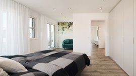 Modernes Schlafzimmer mit gestreiftem Bett, Holzboden, grünem Sofa und geblümter Akzentwand in der Nähe großer Fenster.