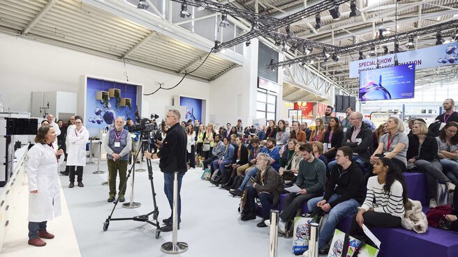 Audience and a man with a camera watch a woman giving a lecture