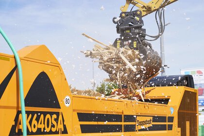 An excavator fills wood waste into a mobile shredder.