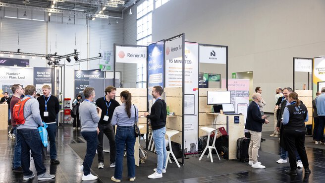Messehalle der digitalBAU mit vielen kleinen Startup-Messeständen, vor denen Besuchende und Ausstellende im Gespräch zusammen stehen.