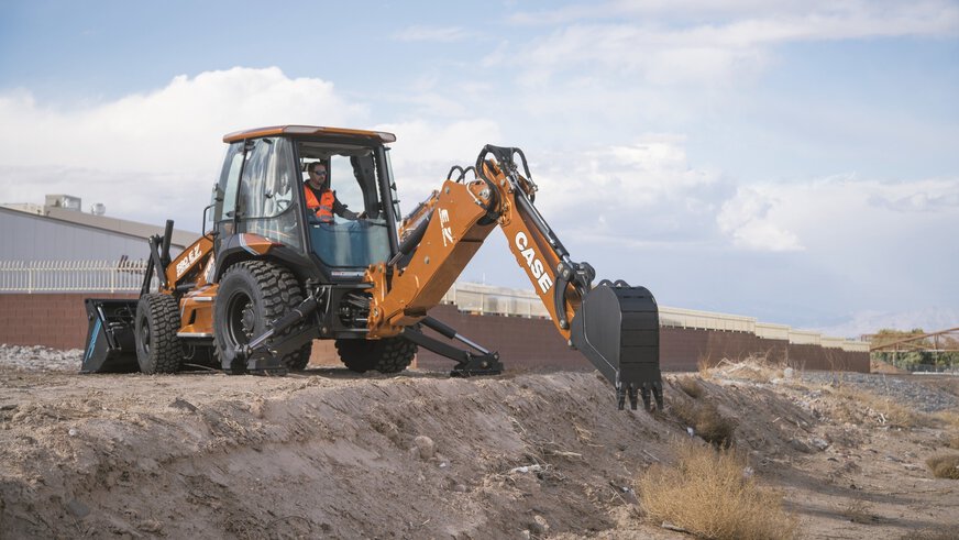 A construction worker operates a CASE backhoe loader on a construction site with a cloudy sky in the background.