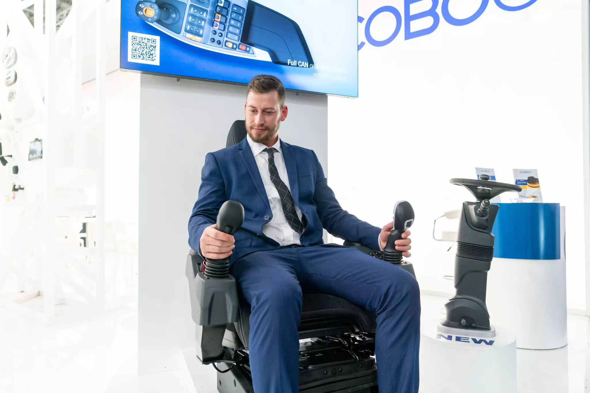 Ein Mitarbeiter am Stand von Cobo auf der bauma 2022 zeigt, wie der neue ergonomische Fahrersitz funktioniert.