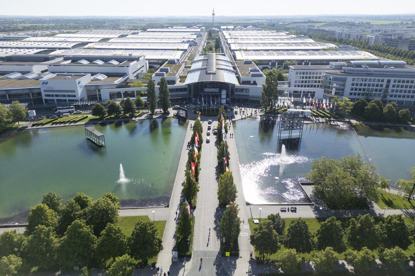 Luftaufnahme eines modernen Ausstellungszentrums mit Springbrunnen, Teichen, Bäumen und großen Gebäuden im Hintergrund.