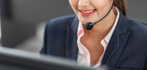 Woman in a suit, smiling and wearing a headset, working on a computer in an office environment