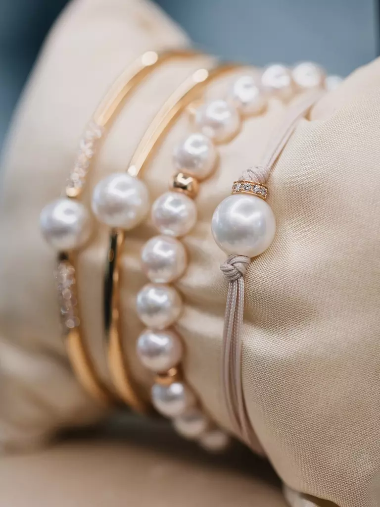 Golden bangles and pearl bracelets on a beige cushion against a soft blue background.