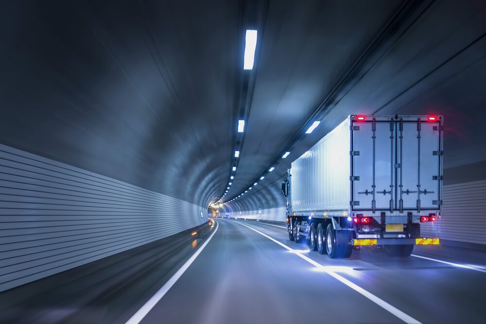 Dynamisches Bild eines weißen LKW's, der durch einen blau beleuchteten Tunnel in eine Kurve fährt.