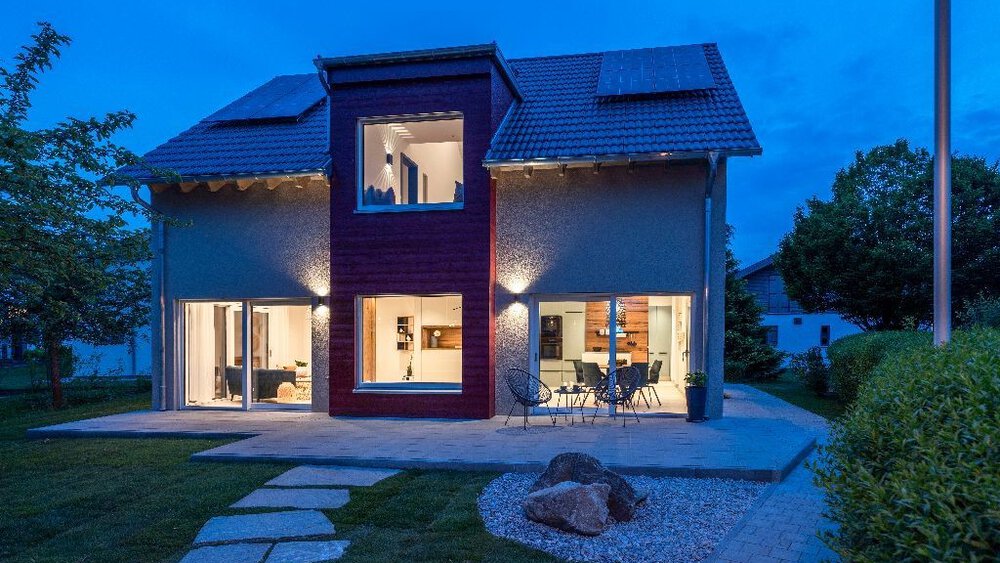 Modernes zweistöckiges Haus mit großen Fenstern, Terrassenmöbeln und einem Gartenweg in der Dämmerung.