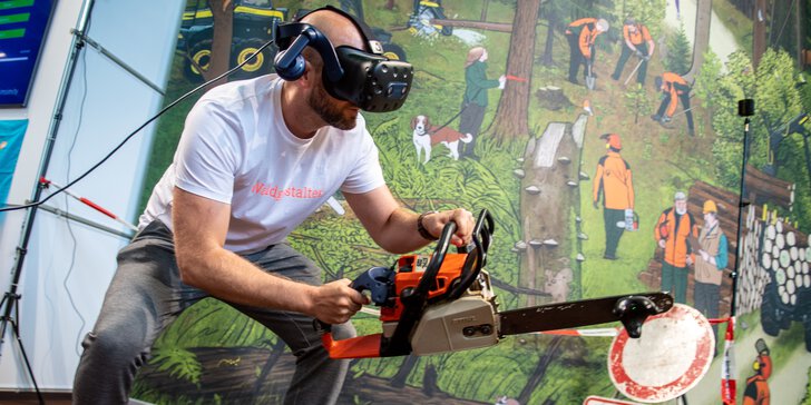 Mann mit VR-Brille simuliert Holzfällarbeit mit Motorsäge in einer interaktiven Messeinstallation vor Waldkulisse.