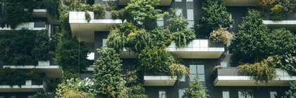 A modern building façade with numerous balconies covered with various lush plants.