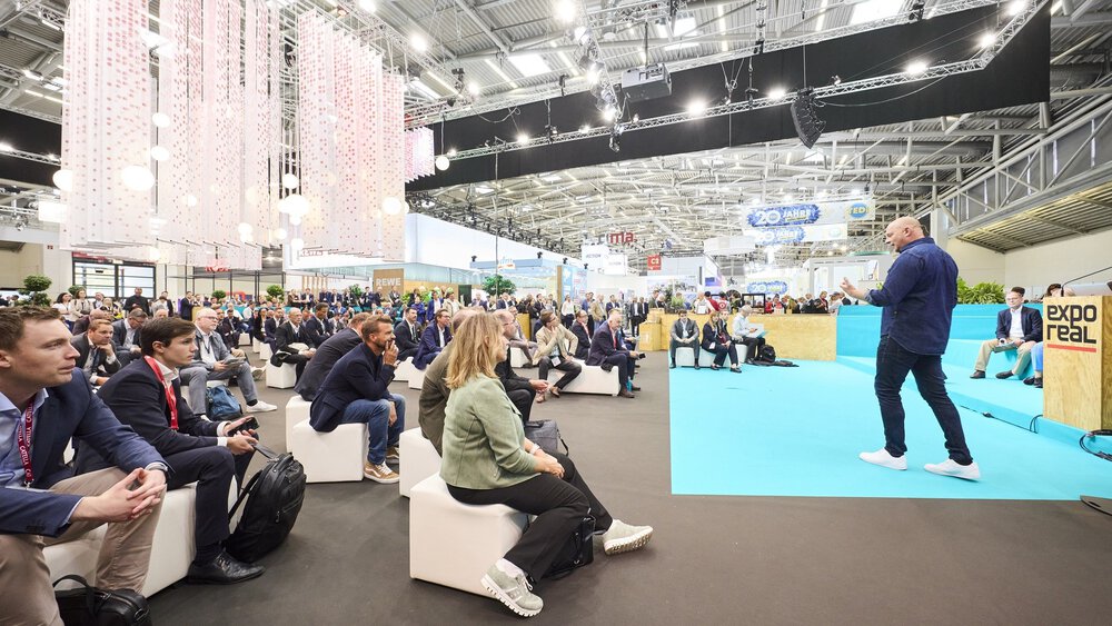 A man speaks to an attentive audience in an exhibition hall at EXPO REAL.
