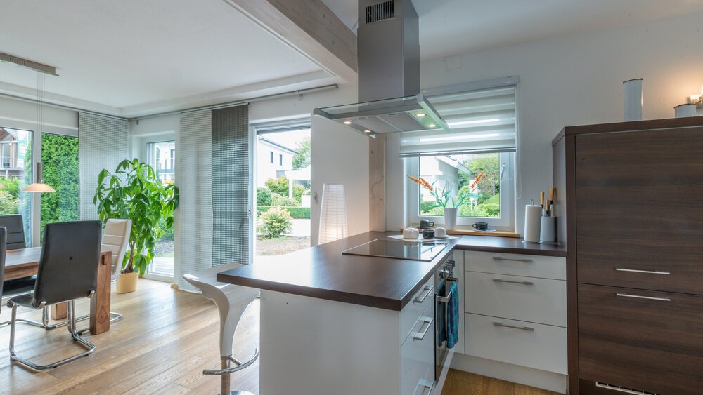 Moderne Küche und Essbereich mit Holzböden, weißen Schränken und großen Fenstern mit Blick auf den Garten.