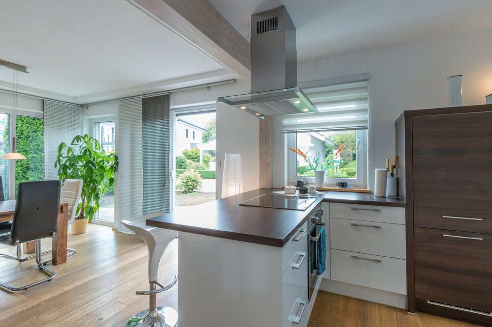 Moderne Küche und Essbereich mit Holzböden, weißen Schränken und großen Fenstern mit Blick auf den Garten.