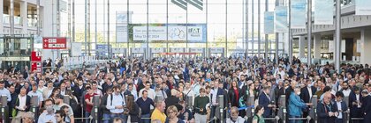 Eine Eingangshalle der Messe München während der IFAT 2022, in der zahlreiche Besucher an den Drehkreuzen für die Ticketkontrolle Schlange stehen.