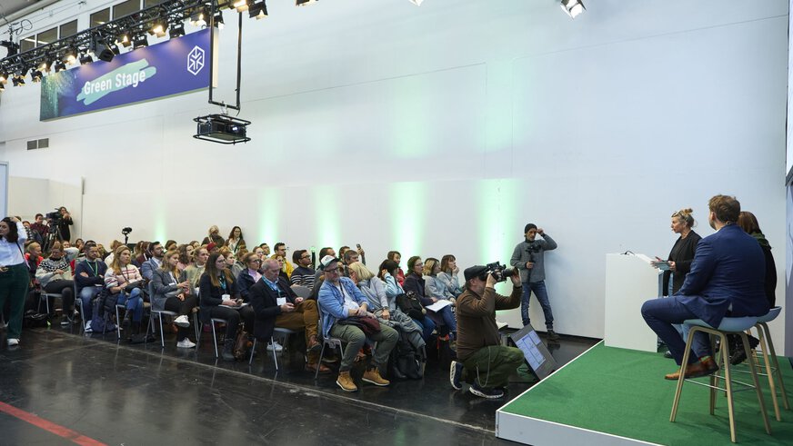 The audience follows a panel discussion with three speakers on a stage in exhibition hall A2.