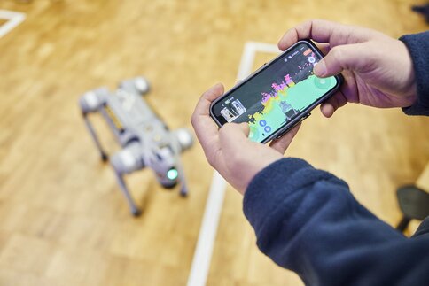 Person controls four-legged robot via smartphone app with environment map.