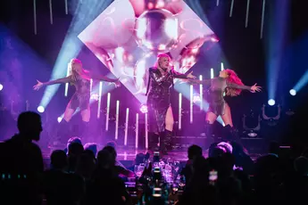 Ásdís appears on stage with two dancers, spotlights illuminate the scene while a rapt audience watches in the foreground.