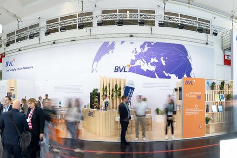 A bustling exhibition stand with people networking and a large world map graphic on the back wall.