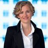 Smiling woman with short blonde hair in a dark blazer and white shirt.