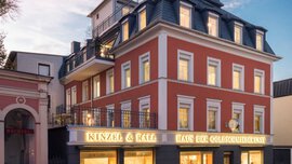 The exterior facade of a jewelry store with a red superstructure and golden shimmering shop windows.