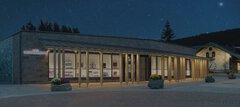 Modernes Gebäude mit Glasfassade und warmem Licht in der Nacht, umgeben von Bäumen und einem Sternenhimmel.