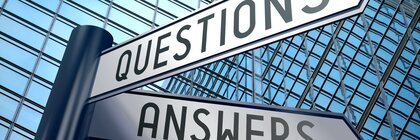 A signpost with two arrows pointing in different directions, labelled ‘Questions’ and ‘Answers’. A reflective building façade can be seen in the background.