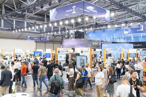 Numerous visitors walk through an exhibition hall with booths beneath the “munich_i” and “AI+Society” banner.