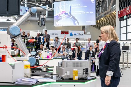 A woman stands in front of a robot-like device. The audience looks at the woman