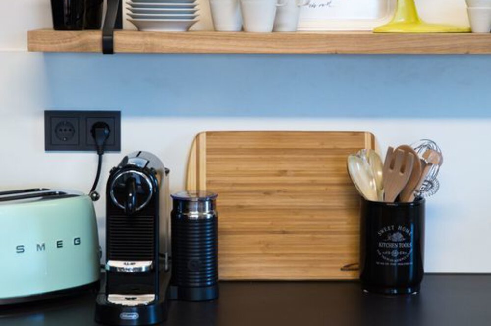 Küchentheke mit Kaffeemaschine, mintgrünem Toaster, Schneidebrett und Utensilienhalter auf mattschwarzer Arbeitsplatte.