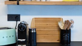 Küchentheke mit Kaffeemaschine, mintgrünem Toaster, Schneidebrett und Utensilienhalter auf mattschwarzer Arbeitsplatte.