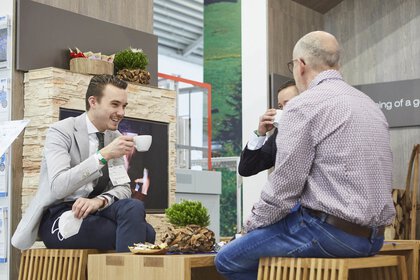 Drei Männer sitzen an einem Tisch, trinken Kaffee und unterhalten sich in einem Bereich der productronica.