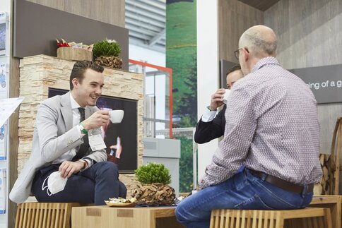 Three men are sitting at a table in one area of productronica, drinking coffee and chatting.