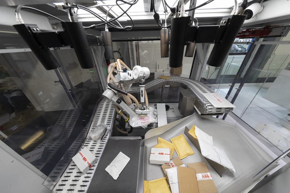 Ein Roboterarm sortiert Pakete in einer modernen Anlage mit Förderbändern und Päckchen in Behältern.