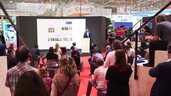 Ein interessiertes Publikum sitzt im Halbkreis auf Sitzwürfeln und einer Holztribüne und lauscht dem Vortrag eines Mannes auf einer Bühne der transport logistic.