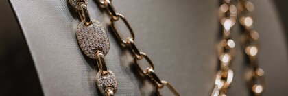 Goldkette mit ovalen, mit Diamanten besetzten Gliedern auf einer grauen Schmuckbüste.