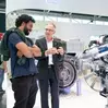 Two men talking in front of a large mechanical component.