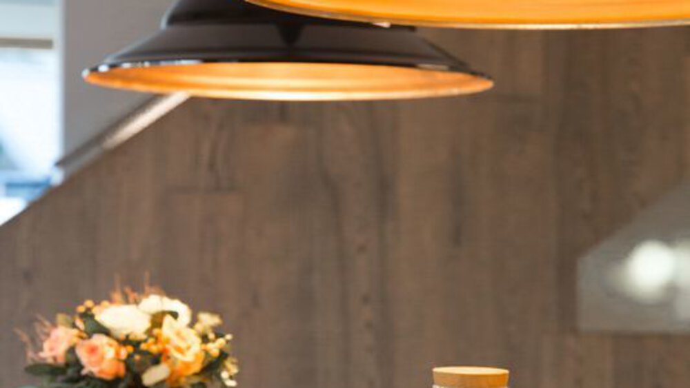 Gemütliches Zimmer mit warmen Hängelampen, einer Blumenvase und einem Glas auf einem Holztisch.