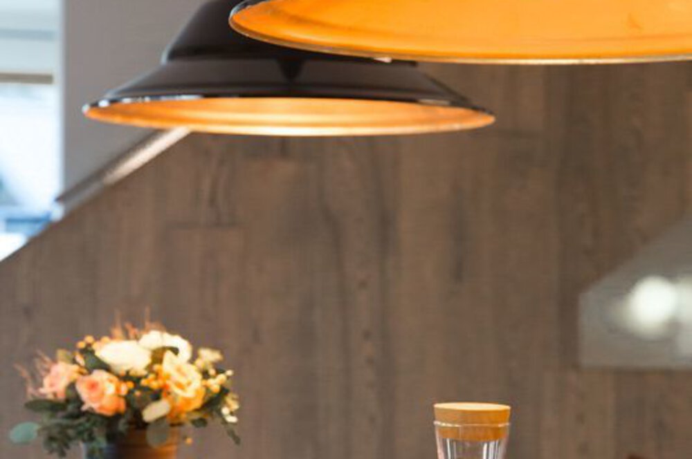 Gemütliches Zimmer mit warmen Hängelampen, einer Blumenvase und einem Glas auf einem Holztisch.