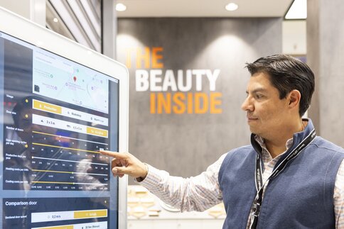A man in business attire interacts with a large touchscreen display; THE BEAUTY INSIDE sign in the background.