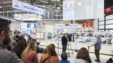 Publikum und ein Mann mit Kamera sehen einer Frau dabei zu, wie sie einen Vortrag hält