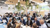 People sitting in groups at the tables of a “German Water Partnership” trade fair stand and chatting.