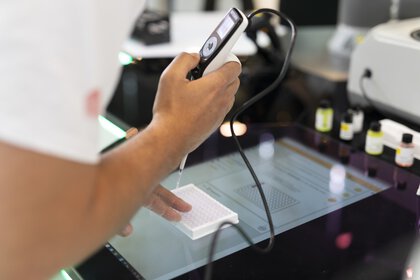 Eine Person hält ein tragbares Messgerät und misst ein rechteckiges Objekt auf einer transparenten Glasoberfläche.