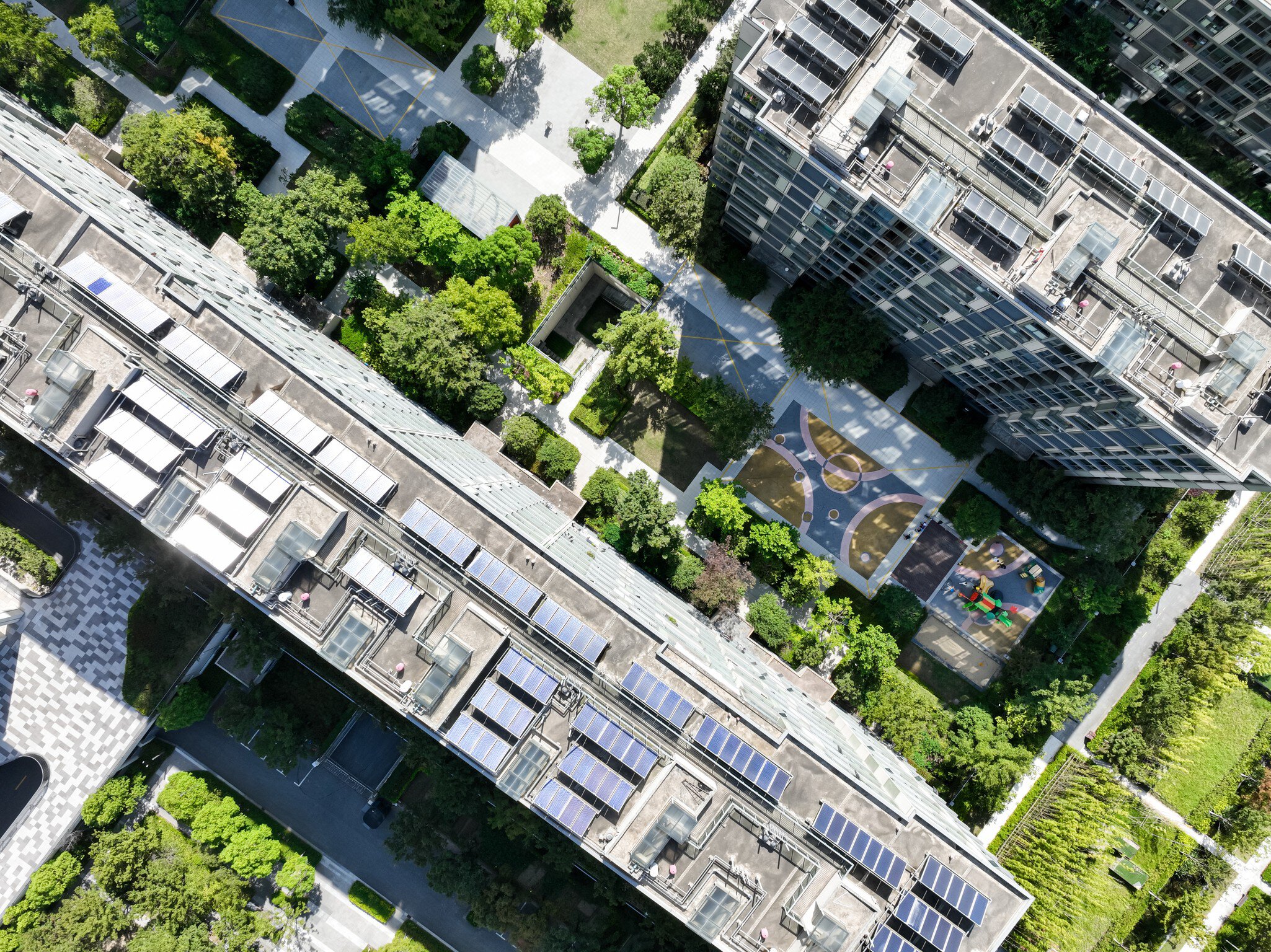 Luftaufnahme mehrerer städtischen Wohnkomplexes mit Solarmodulen und von Bäumen und Wegen umgebenen Innenhöfen.