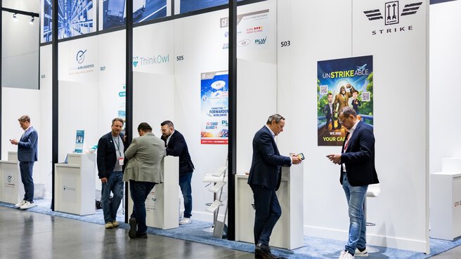 People socialize and chat at a trade fair booth decorated with “Made in Germany” signs and advertising posters.