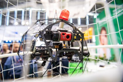 Close-up of a drone with a red camera, sensors and a protective cage on display in an exhibition hall.