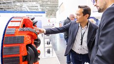 Two men inspect a large red machine part at bauma.