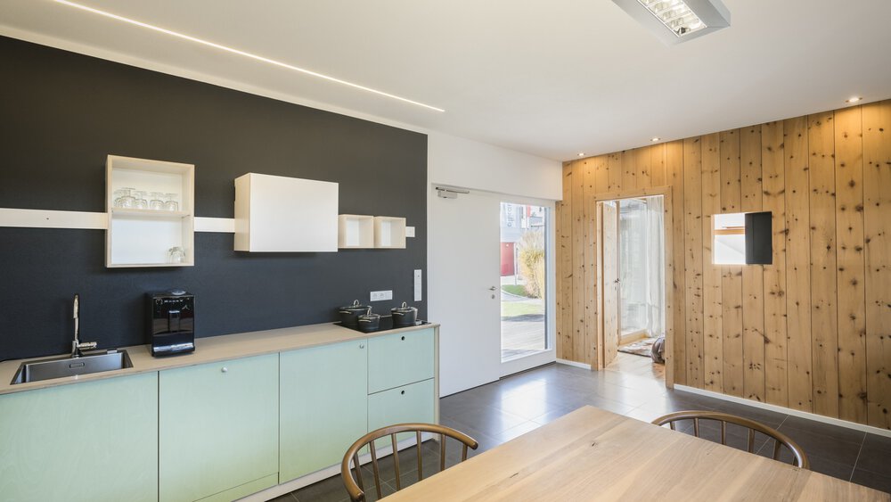 Minimalistische Küche und Essbereich mit schwarzen Wänden und Holzakzenten, hellen Holzmöbeln und modernen Geräten.