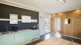 Minimalistische Küche und Essbereich mit schwarzen Wänden und Holzakzenten, hellen Holzmöbeln und modernen Geräten.