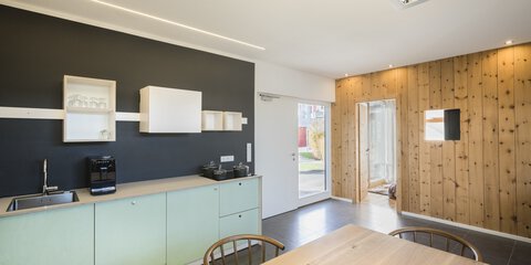 Minimalistische Küche und Essbereich mit schwarzen Wänden und Holzakzenten, hellen Holzmöbeln und modernen Geräten.