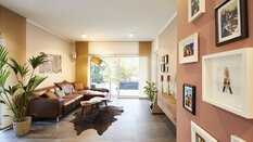 Modernes Wohnzimmer mit braunem Sofa, Pflanzen, Wandkunst und einem Fenster mit Blick nach draußen.