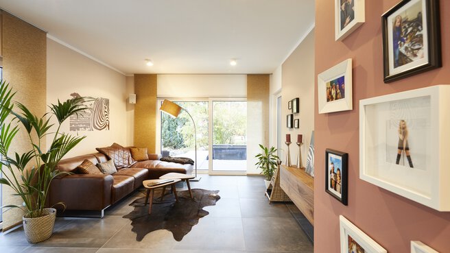 Modernes Wohnzimmer mit braunem Sofa, Pflanzen, Wandkunst und einem Fenster mit Blick nach draußen.